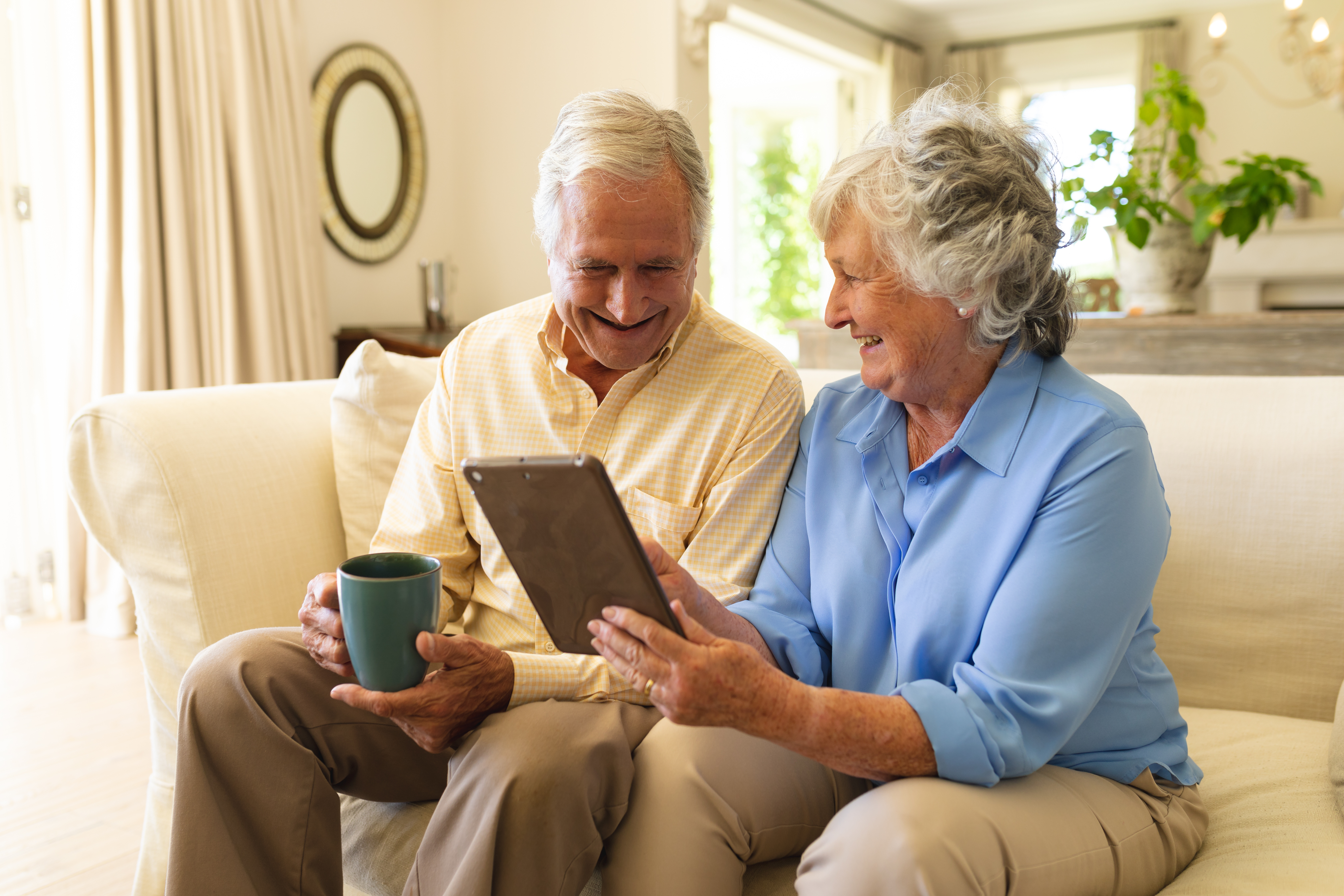 couple de séniors consultant une tablette et un téléphone assis sur un canapé